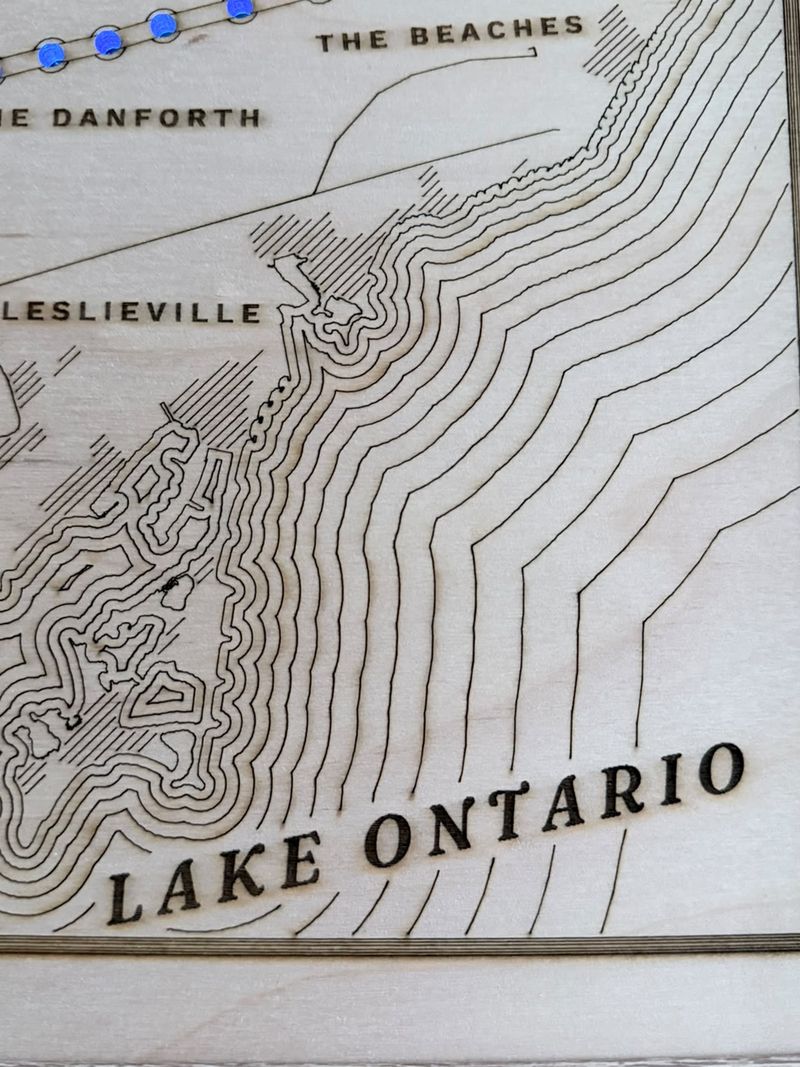 Close-up of Lake Ontario engraved as rippling contour lines around the Leslie Street Spit, below The Beaches, The Danforth and Leslieville