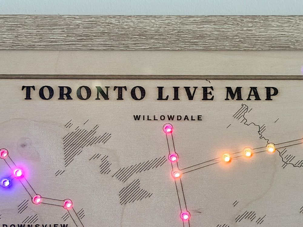 Close-up of the engraved title, Toronto Live Map, above Willowdale, with pink and orange station lights set into the birch